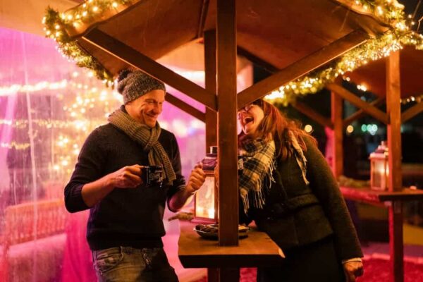 Zwei Personen stehen an einem Tisch auf dem Weihnachtsmarkt im Dock 10 und lachen.